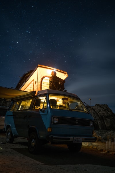 一名男子坐在蓝色货车的顶部，在夜间凝视天空